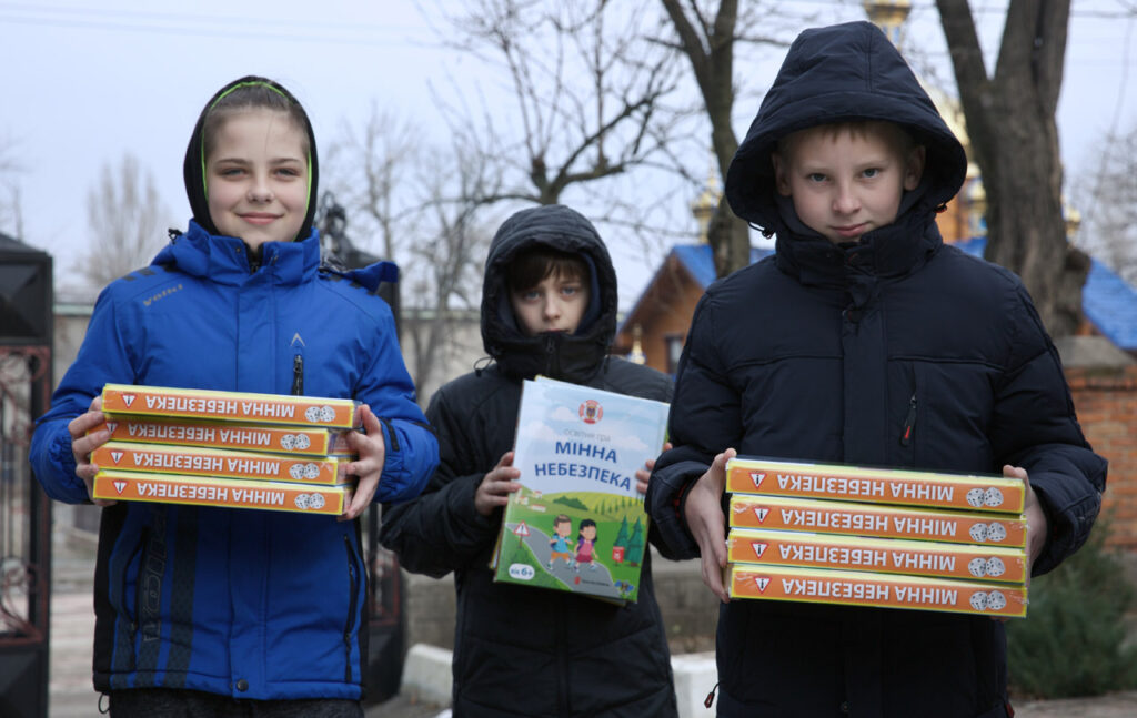 троє дітей на вулиці в зимовому одязі тримають коробки з Грою "Мінна небезпека"