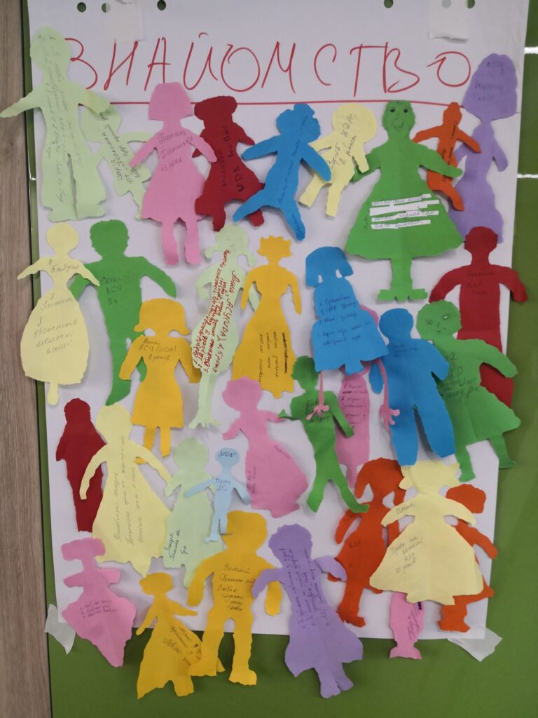 паперова дошка, на яку наклеєні паперові різнокольорові фігурки людей, зроблені дітьми